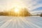 Winter landscape at sunset: bright sunshine breaking through the tree branches