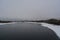 Winter landscape with unfrozen river and town on the bank in cloudy day