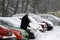 Winter. A man with a broom cleans car from snow on the street after big snowstorm in the city, all cars under snow, icy roads, sno