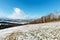 Winter mountain landscape with field, grove and village in far