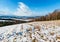 Winter mountain landscape with field, grove and village in far