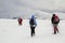 Winter mountain landscape. Three travelers tourist hikers in bright clothing with backpacks on snowy field walking towards