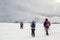 Winter mountain landscape. Three travelers tourist hikers in bright clothing with backpacks on snowy field walking towards