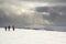 Winter mountain landscape. Three travelers tourist hikers in bright clothing with backpacks on snowy field walking towards