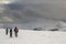 Winter mountain landscape. Three travelers tourist hikers in bright clothing with backpacks on snowy field walking towards