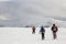 Winter mountain landscape. Three travelers tourist hikers in bright clothing with backpacks on snowy field walking towards