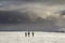 Winter mountain landscape. Three travelers tourist hikers in bright clothing with backpacks on snowy field walking towards