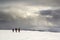 Winter mountain landscape. Three travelers tourist hikers in bright clothing with backpacks on snowy field walking towards