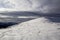 Winter mountain landscape. Wide view of mountain covered with shiny snow and small silhouettes of travelers tourist hikers under c