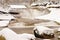 Winter at mountain river. Big stones in stream covered with fresh powder snow and lazy water with low level.