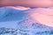 Winter mountains ridge in pink sunrise colors, hills covered by white snow