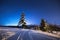 Winter night scenery. Winter road on mountain hills under blue night sky full of stars. Winter mountain nature