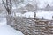 Winter old shabby wobbly wicker fence made of wooden boards. Snow blizzard