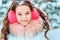 Winter portrait of happy kid girl in pink earmuffs walking outdoor in snowy winter forest