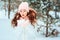 Winter portrait of happy kid girl in white coat and hat and pink mittens playing outdoor in snowy winter forest