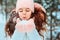 Winter portrait of happy kid girl in white coat and hat and pink mittens playing outdoor in snowy winter forest and blowing snow