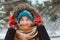 Winter portrait of happy young woman walking in snowy forest in warm outfit,