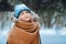 Winter portrait of happy young woman walking in snowy forest in warm outfit, knitted hat and oversize scarf