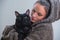 Winter portrait of young kind woman holding big black cat