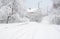 A winter road in a country, town after a heavy snow storm with broken, damaged trees covered with snow and unplowed road