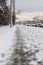 Winter road with melting from salt snow. Sidewalk along highway with cars on snowy evening