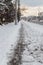 Winter road with melting from salt snow. Sidewalk along highway with cars on snowy evening