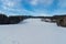 Winter rolling landscape with snowcapped meadow, few houses, forest and blue sky with clouds