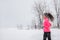 Winter running woman in cold snow weather jogging outside wearing windproof clothes with gloves, headband, winter tights and wind