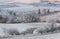 Winter Rural Landscape With With Frosted Wavy Plowed Fields, Trees In Hoarfrost And Old Windmill On The Hill. Beautiful Morning On