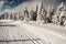 Winter scenery with prepared cross-country skiing track, frozen trees and blue sky with clouds