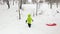 Winter side follow little child pulling red bobsled on snowy field.son or daughter, bobsleigh on snow.Family people have