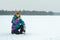 Winter sitting on haunches hiker with metal drink flask resting at snowy landscape background