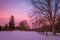 Winter snow at dusk fills the sky with beautiful tones of violet in a fence-lined park