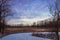 Winter snow at dusk fills the sky with beautiful tones of violet over a wooded field