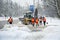 In winter, in snowstorm, workers and a tractor clean the road fr