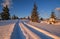 Winter snowy hills, tracks on rural dirt road and trees in last evening sunset sun light. Small and quiet alpine village outskirts