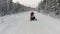 Winter snowy landscape with road and snowmobile riding along spruce tree forest. Clip. Concept of winter sports