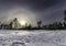 Winter Sun halo just above wild Scandinavian pine forest at early spring, crust of snow. Blue sky with old chemtrails