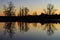 Winter sunset. Leafless trees reflected in a lake