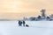Winter travelers hiking on lake ice at sunset over a village