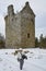 A Winter Walker passing by Invermark Castle in Glen Esk, with the path covered in snow.