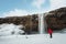 Winter waterfall landscape, photographer in red jacket taking photograph with camera tripod at Seljalandsfoss waterfall in Iceland