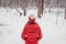 Winter woman walking in snow covered woods park. forest trail outdoors. View from behind of woman in red coat and beanie