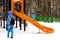 Wintertime. Mom watching little kid sliding the slide on the playground