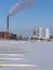 A wintery scene of an urban powerplant with frozen lake in the foreground