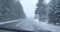 Wipers cleaning windshield as car driving along north snowy road. Driver`s POV of travelling in severe northern country