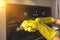 Wiping and cleaning oven door at home kitchen with yellow rubber glove and sponge