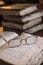 Wire framed reading glasses on resting on pages of open book with vintage, old books in background