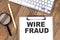 WIRE FRAUD text on paper clipboard with magnifier and keyboard on wooden background