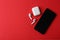 Wireless earphones, mobile phone and charging case on red background, flat lay